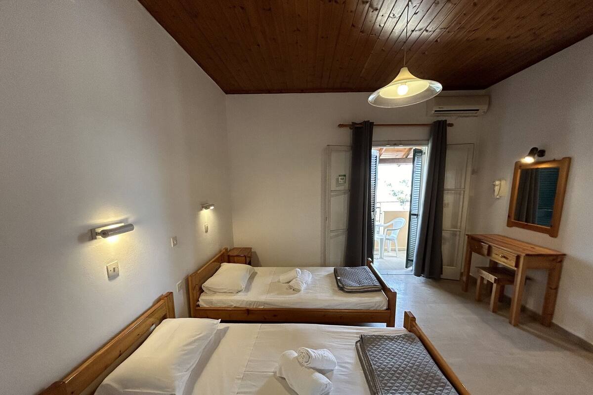 A room with two wooden beds, a small wooden table, a mirror, and a ceiling light.