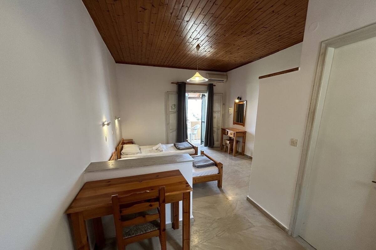 A room with a wooden ceiling, a bed, a desk, and a chair.