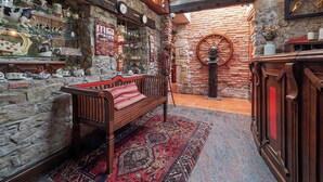 A rustic interior with stone walls, a wooden bench, a red patterned rug, and a variety of decorative items including clocks and pottery. - Don Pedro (Aviles)