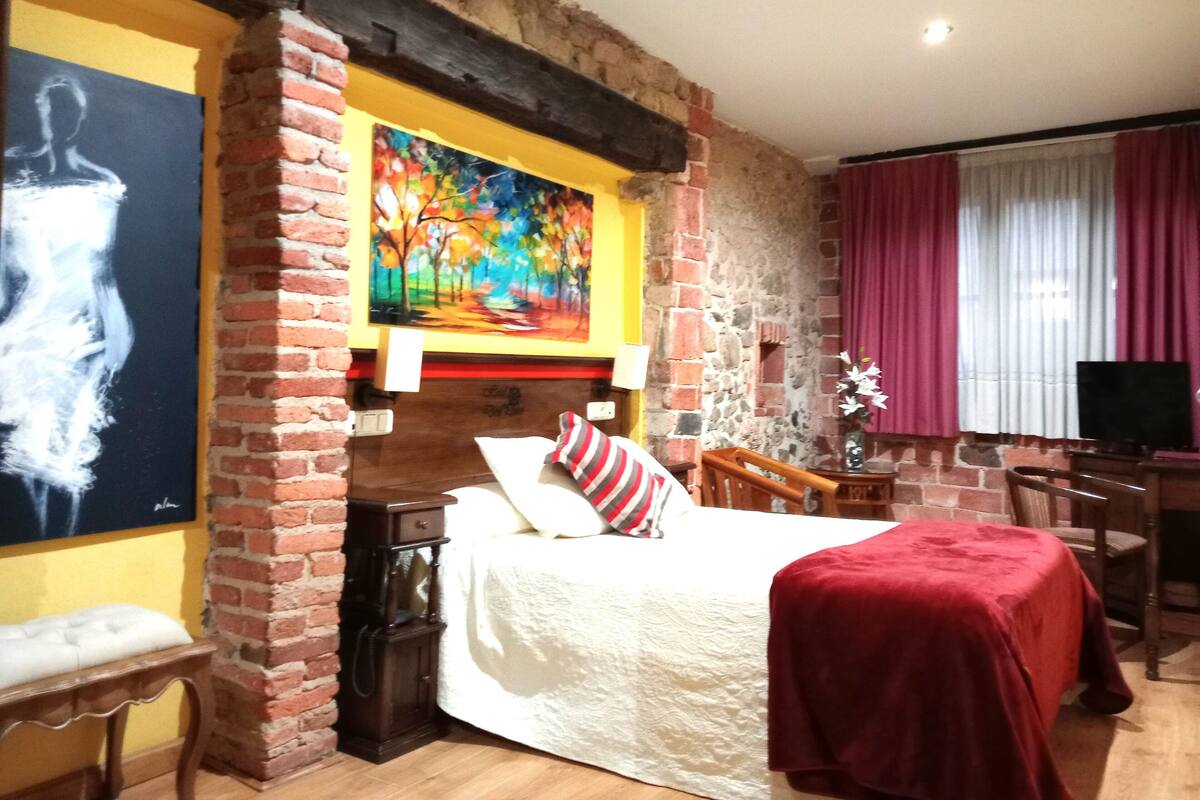 Una habitación con cama, escritorio, silla, televisor y un cuadro en la pared.