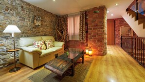 A cozy living room with a stone wall, a wooden floor, a sofa, a coffee table, and a staircase. - Don Pedro (Aviles)