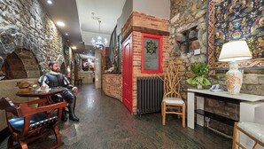 A narrow corridor with stone walls, a red door, and a chandelier. There is a table with a chair and a lamp. - Don Pedro (Aviles)