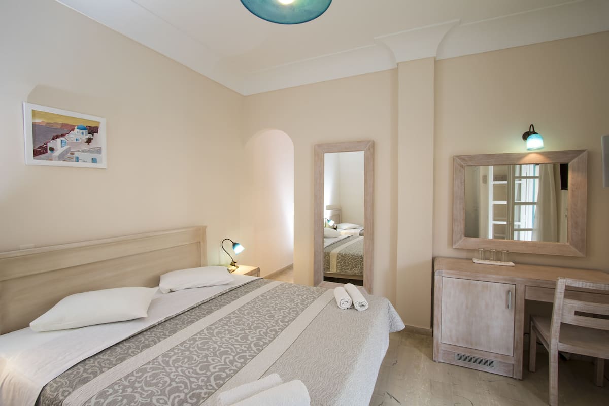 Une chambre d’hôtel comprenant un lit, une table de chevet, un miroir et un petit bureau avec une chaise.