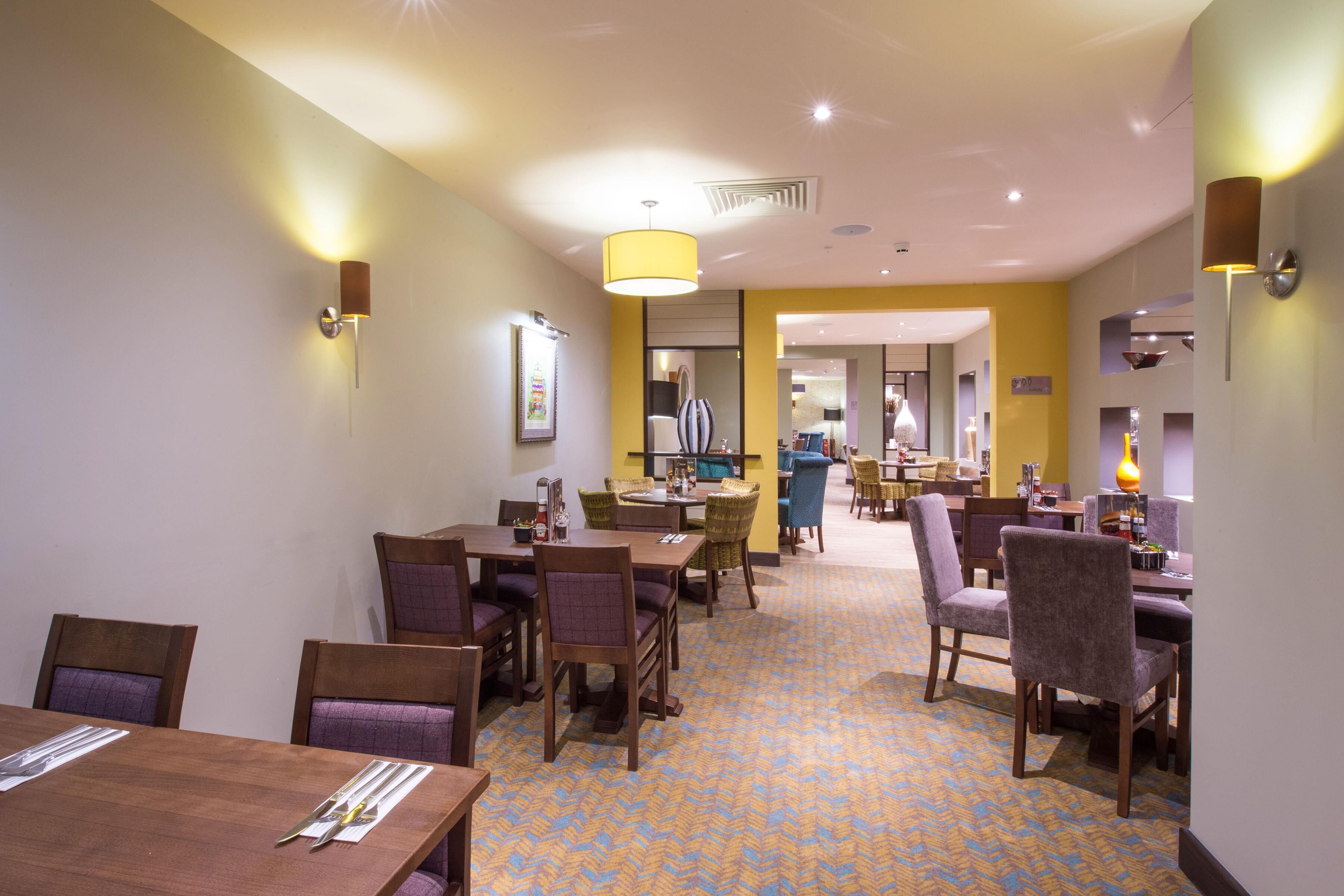 A dining area with tables and chairs, a patterned carpet, and wall-mounted lighting fixtures.