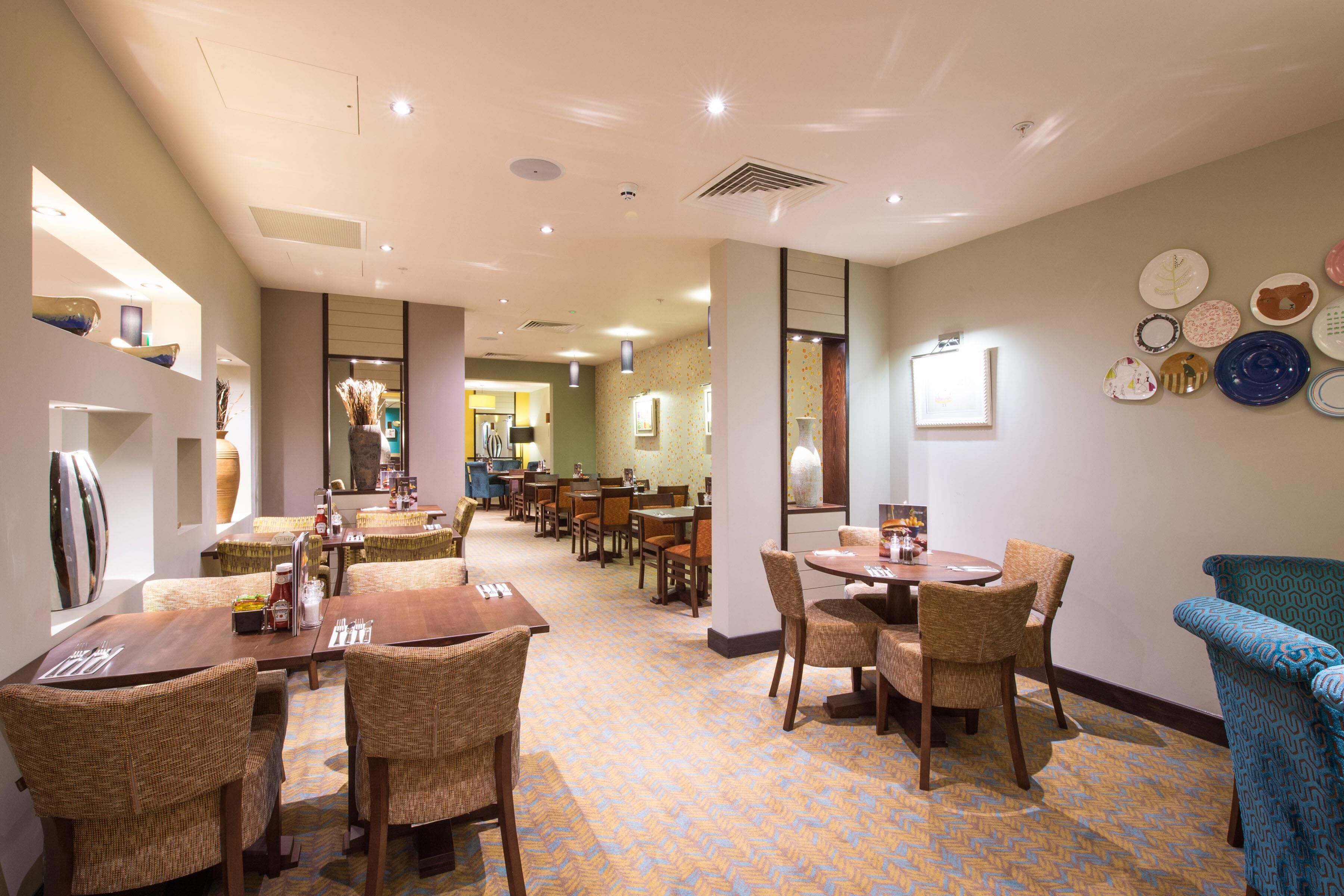 A hotel dining area with multiple tables and chairs, a patterned floor, and wall-mounted plates.