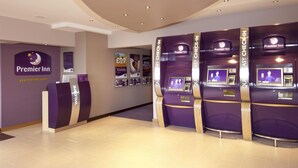 Ein Empfangsbereich eines Premier Inn mit einer Rezeption, Selbstbedienungsterminals und einem Schreibtisch.