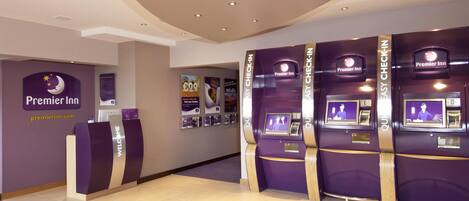 A Premier Inn reception area with a check-in counter, self-service kiosks, and a reception desk.