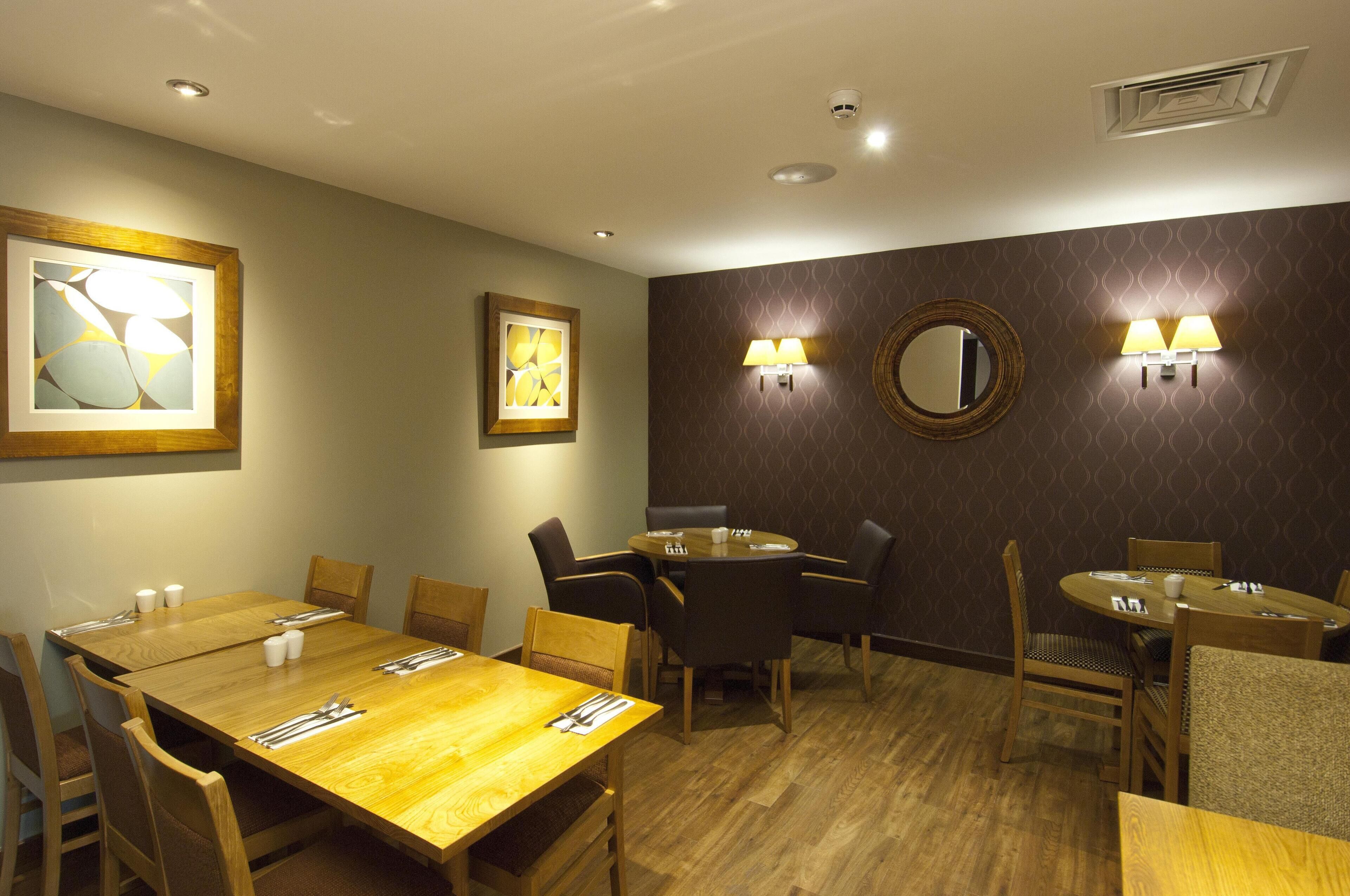 Habitación de hotel con comedor que incluye mesas y sillas de madera, obras de arte colgadas en la pared y apliques.