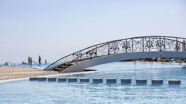 A swimming pool with a decorative bridge and a beach area.