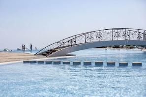 Una piscina con un puente decorativo y una zona de playa.