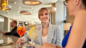A person in a checkered blazer sitting at a table with a drink.