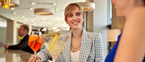 A person in a checkered blazer sitting at a table with a drink.