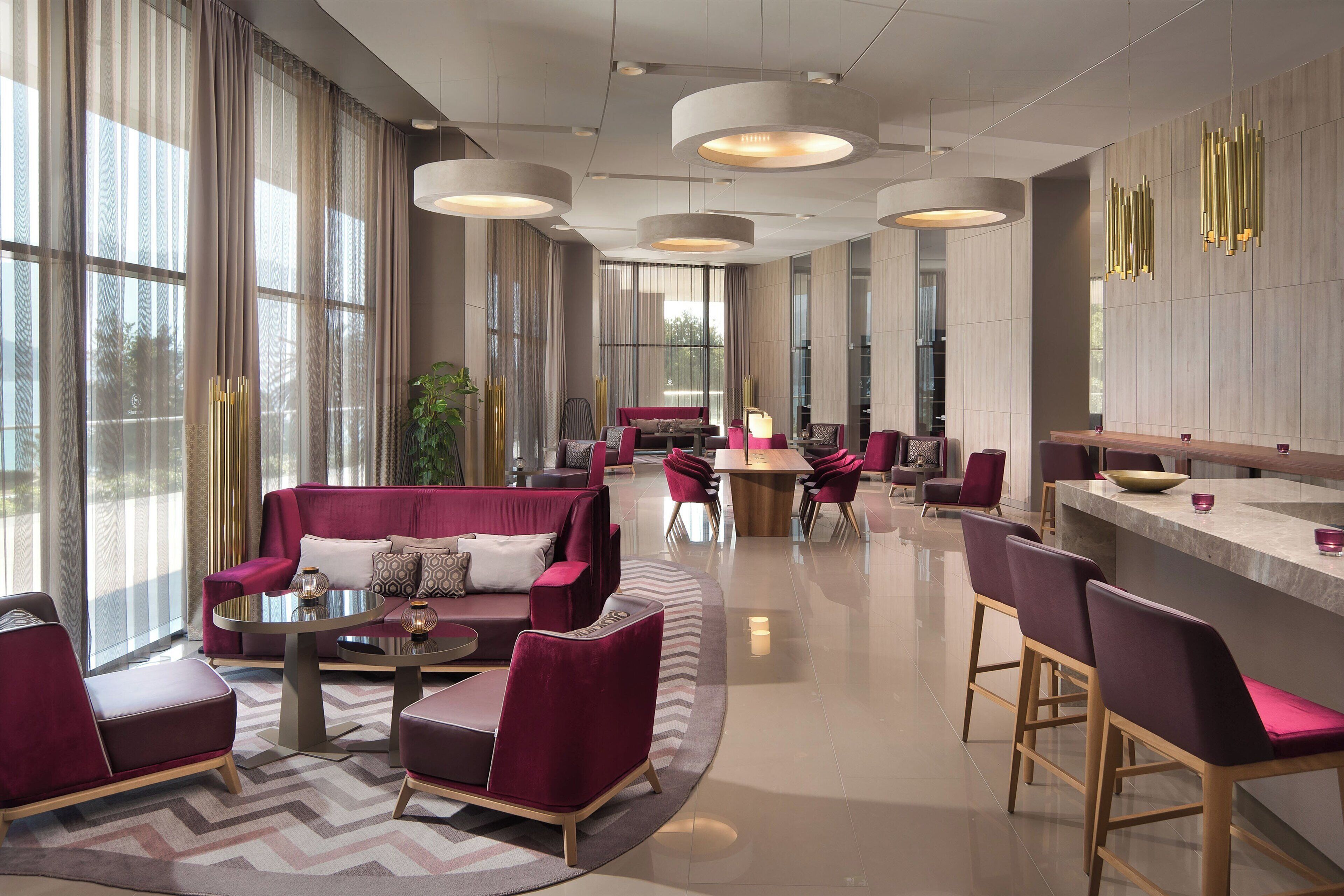 A modern hotel lobby with a seating area, a bar, and large windows.