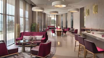 Un vestíbulo de hotel moderno con zona de estar, bar y amplios ventanales.