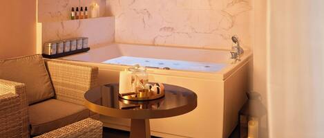 A bathroom with a bathtub, a small round table with toiletries, and a wicker chair.