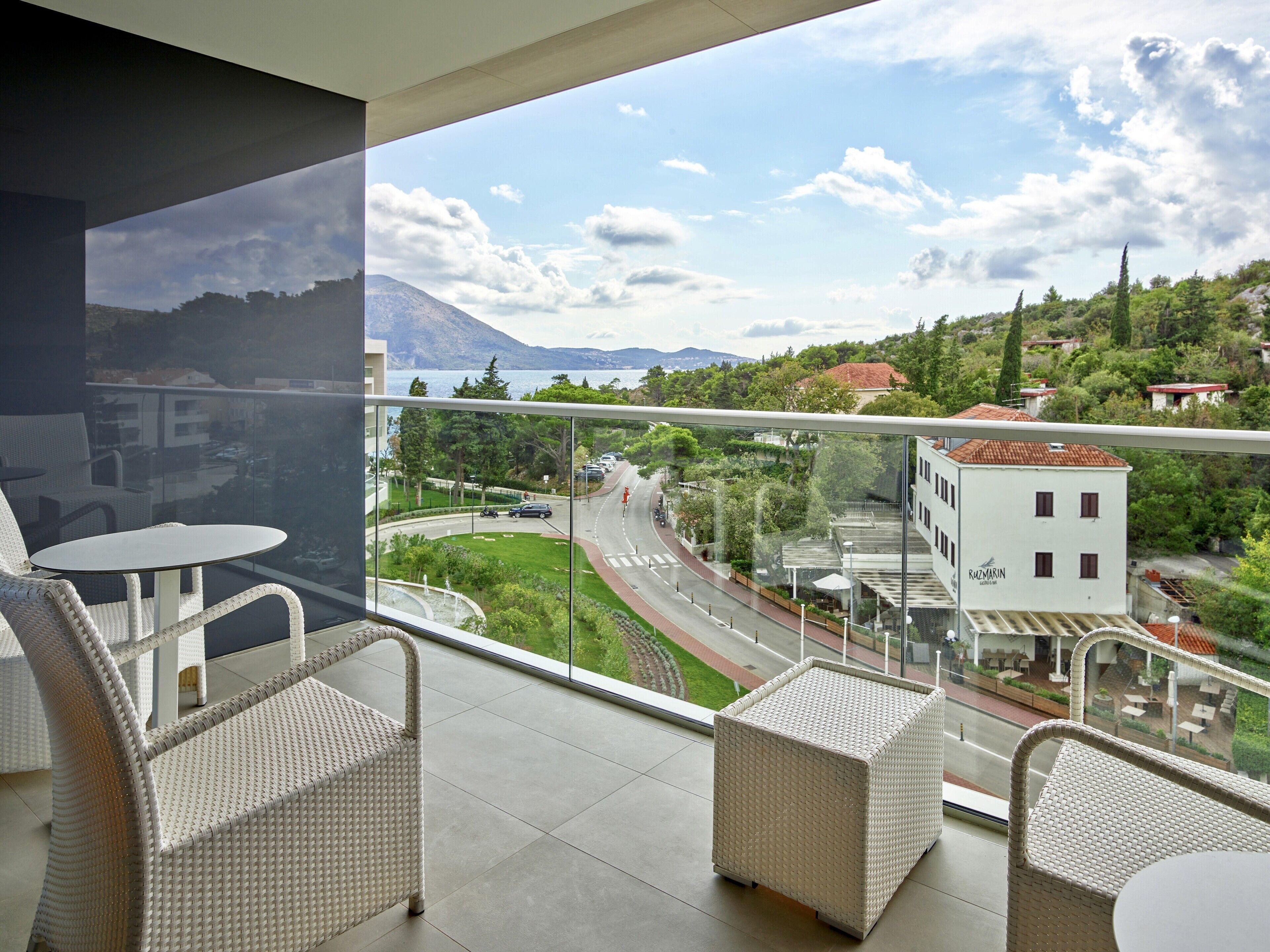 A balcony with wicker furniture and a view of a road, buildings, and mountains.