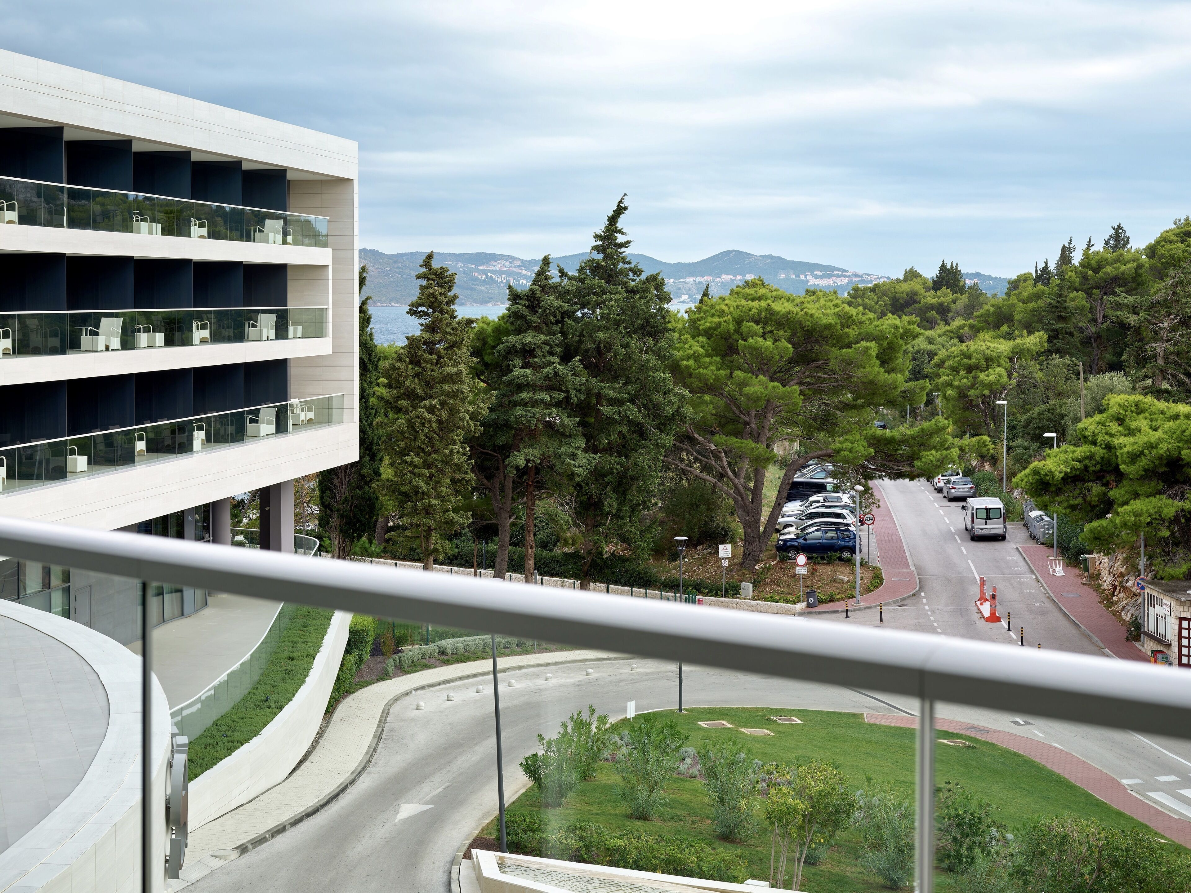 Un edificio moderno con diversi piani, una strada ad arco e vista su una strada con auto parcheggiate e alberi.