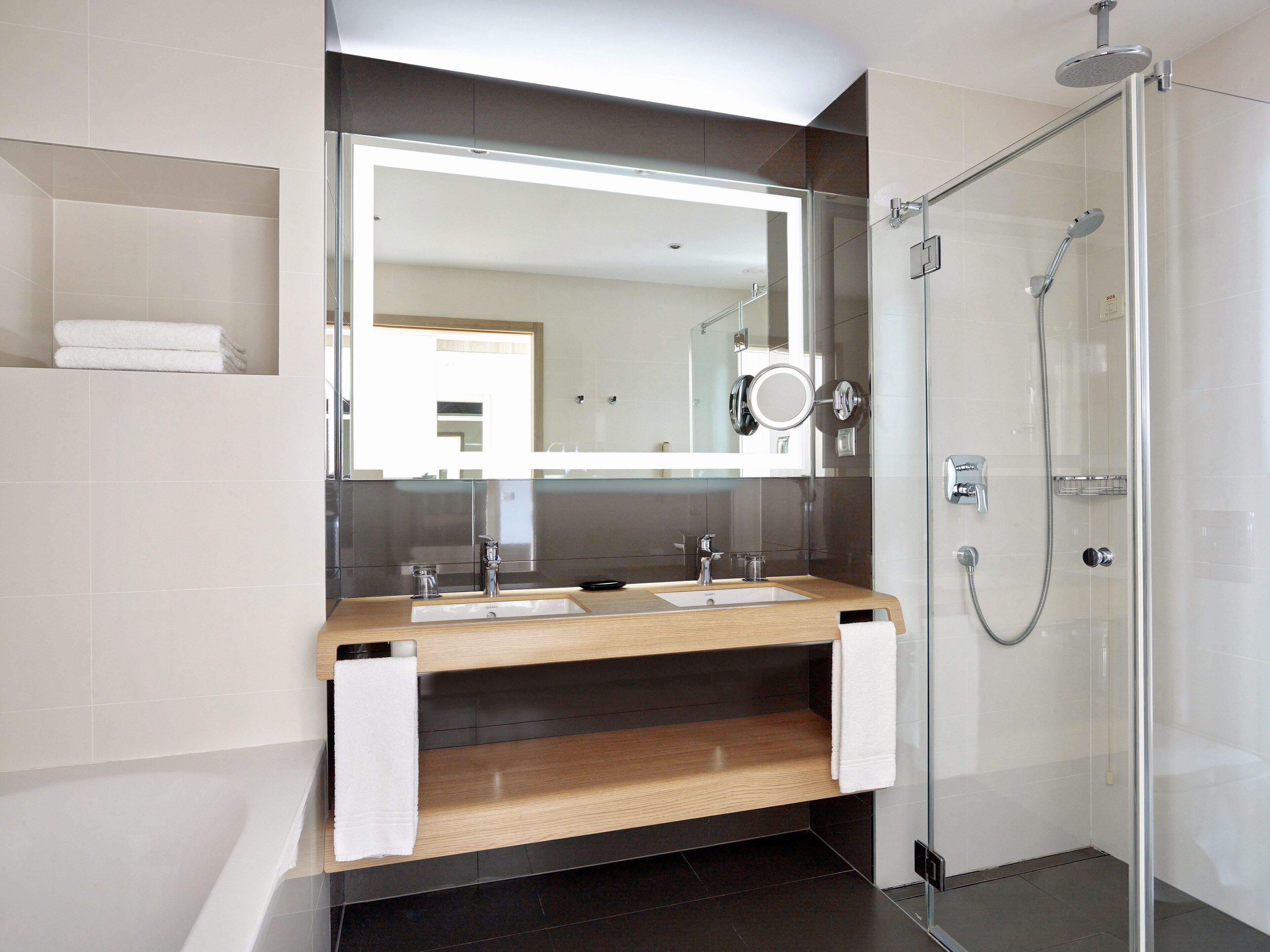 Een moderne badkamer met een douchecabine van glas, een wastafel met twee kommen en een grote spiegel.