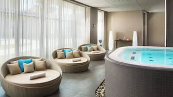 Un espace bien-être comprenant un jacuzzi, des canapés en osier avec des coussins et une grande fenêtre agrémentée de rideaux légers.