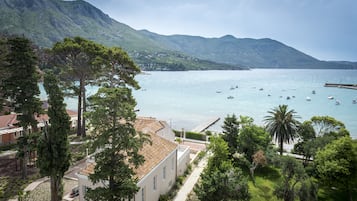 Una vista costiera con montagne sullo sfondo, un porto turistico con barche e edifici in stile mediterraneo.