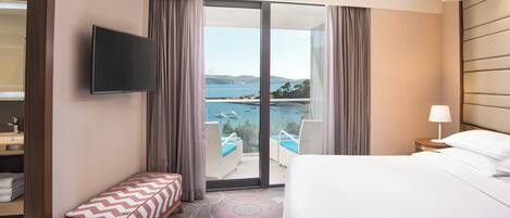 A hotel room with a bed, a TV, a bench, a view of a pool and mountains.