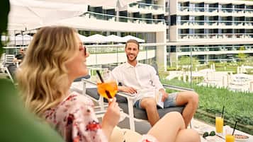 Um casal sentado em mesa ao ar livre, com vista para um edifício moderno e vegetação.