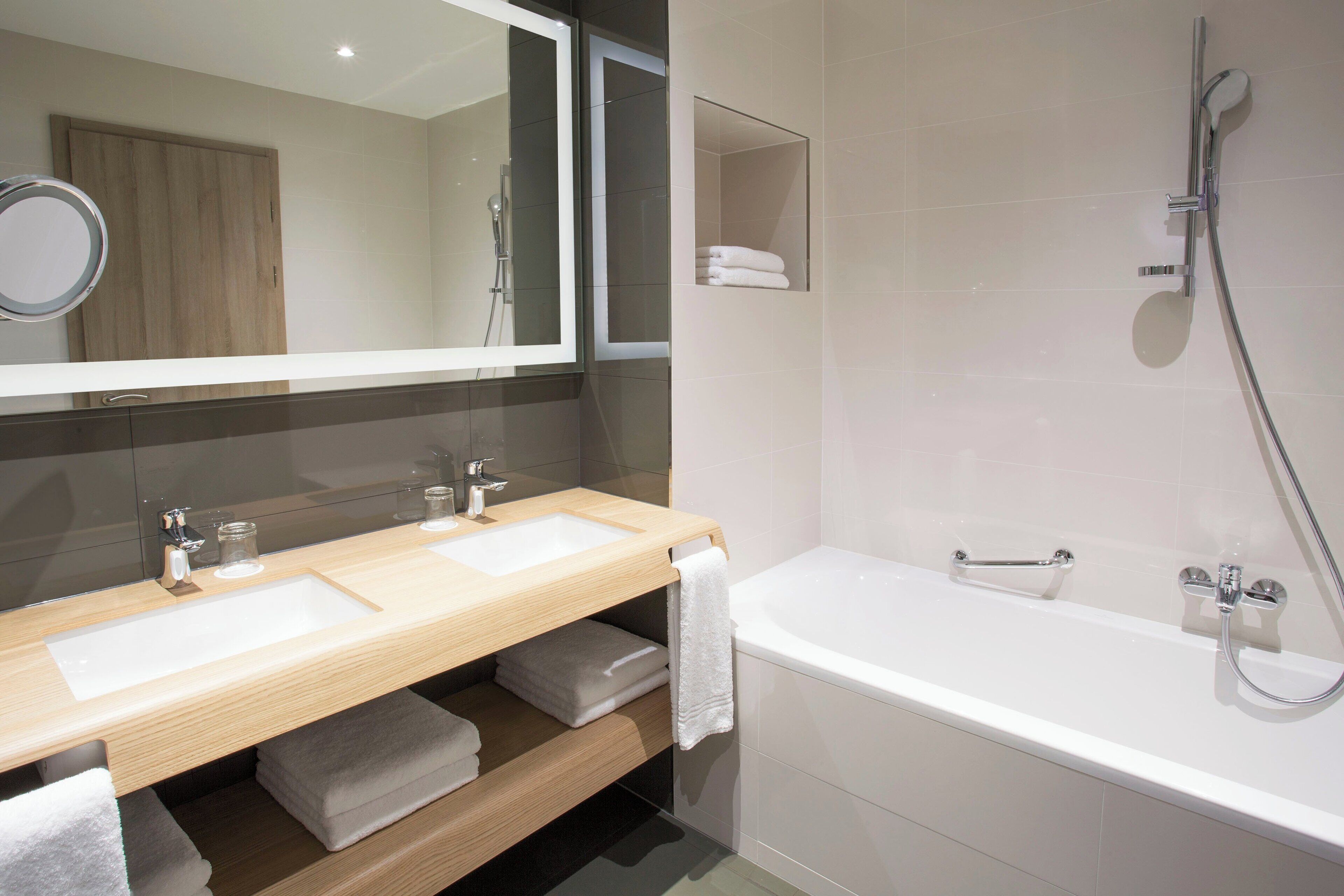 A modern bathroom with two sinks, a large mirror, a bathtub, and a shower.