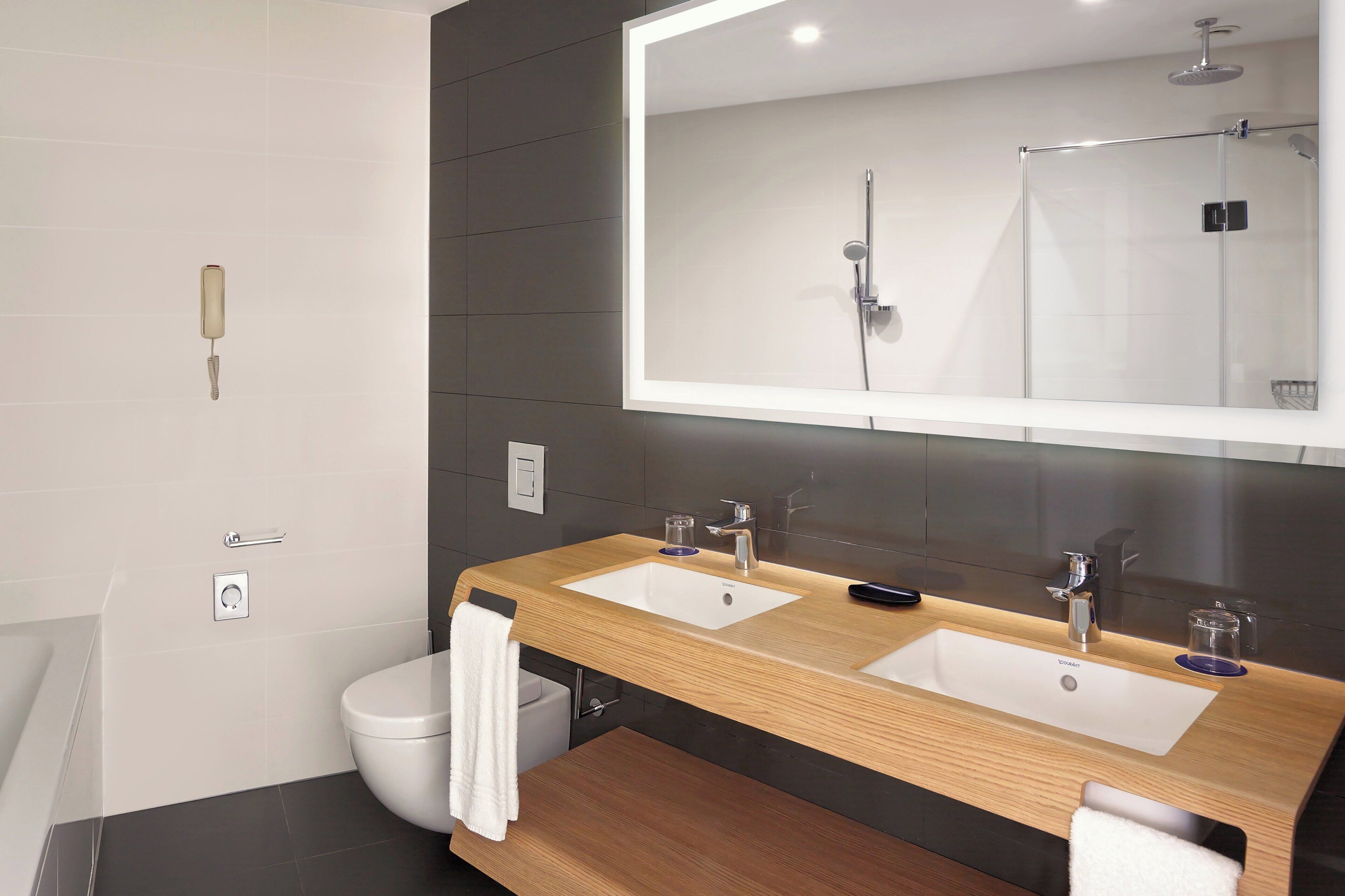A modern bathroom with two sinks, a large mirror, and a shower.