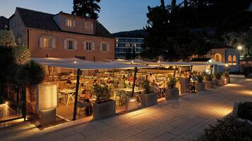 An outdoor dining area with tables and chairs, surrounded by potted plants and a covered seating area.
