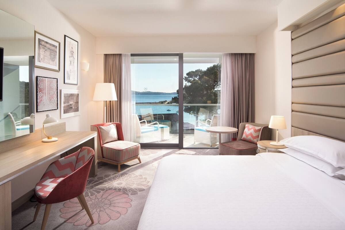 Une chambre d’hôtel équipée d’un lit, d’un bureau, d’une chaise et d’un balcon avec vue sur la mer.