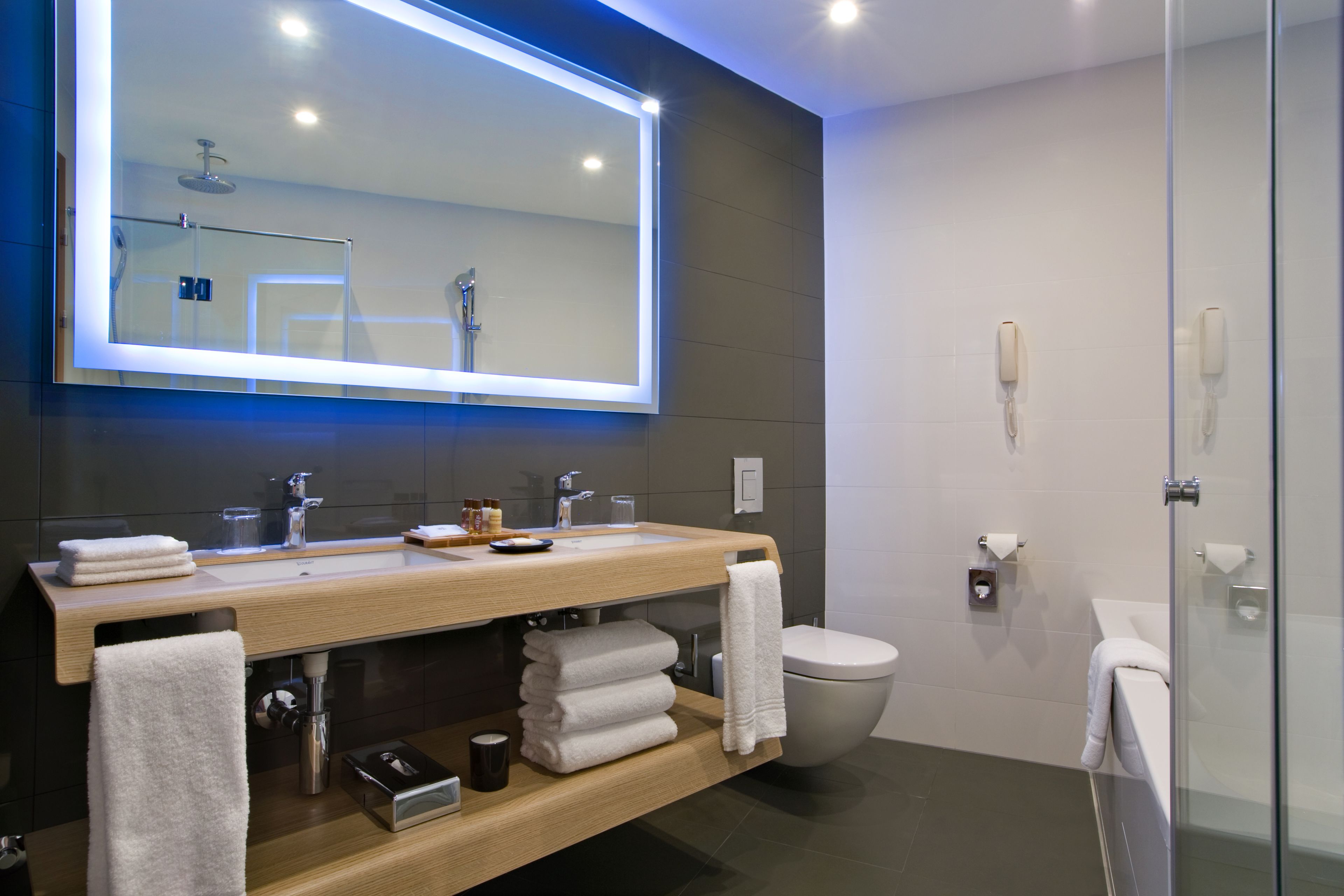 Un baño moderno con un espejo grande, dos lavamanos, un inodoro y una cabina de ducha de vidrio.