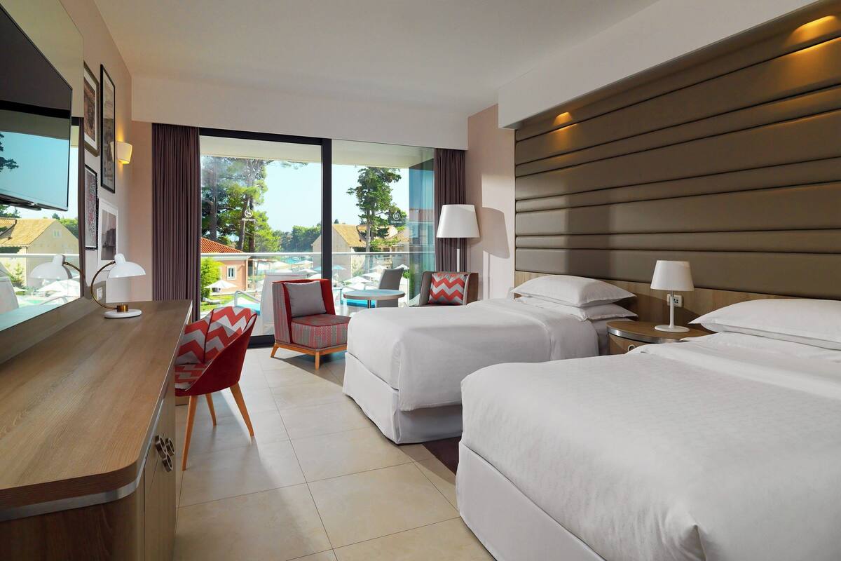 Une chambre d’hôtel avec deux lits, un bureau, une chaise et un balcon avec vue.