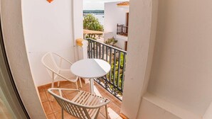 A balcony with a white table and chairs, a view of the sea, and a small orange lantern. - Hostal LA Savina (Formentera)