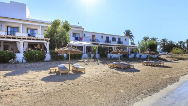 A beachside hotel with sun loungers, umbrellas, and a white building with balconies. - Hostal LA Savina (Formentera)