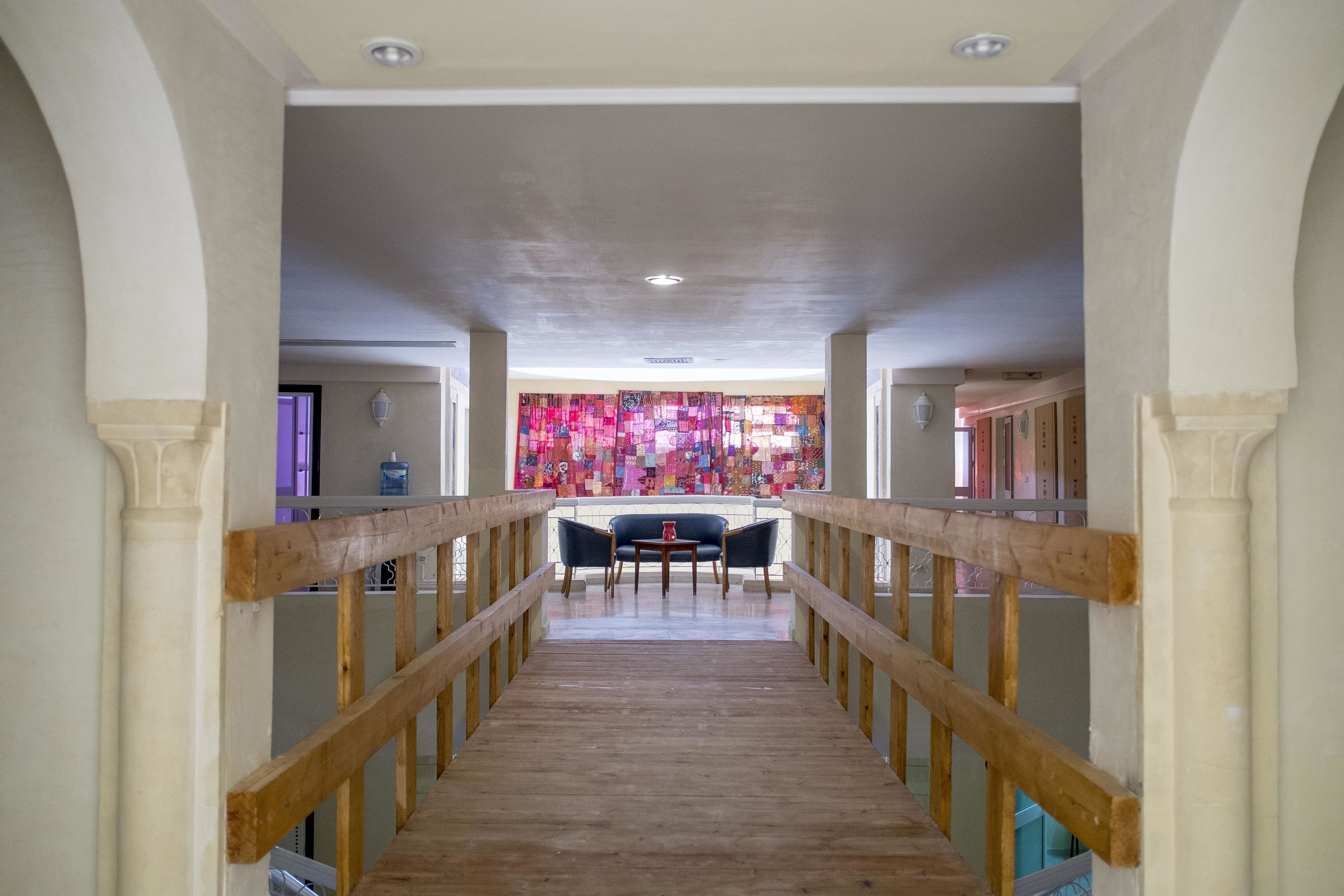 A wooden staircase with a railing leading to a room with a colorful tapestry and a table with chairs.