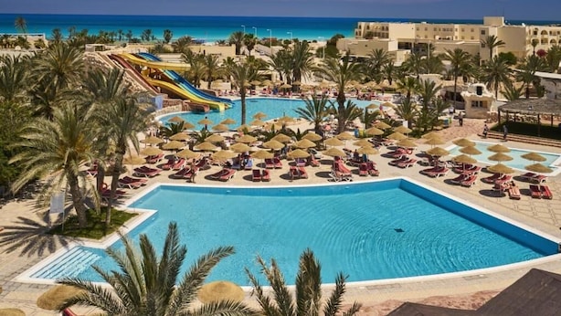 Et resort med en stor swimmingpool, palmer og havudsigt.