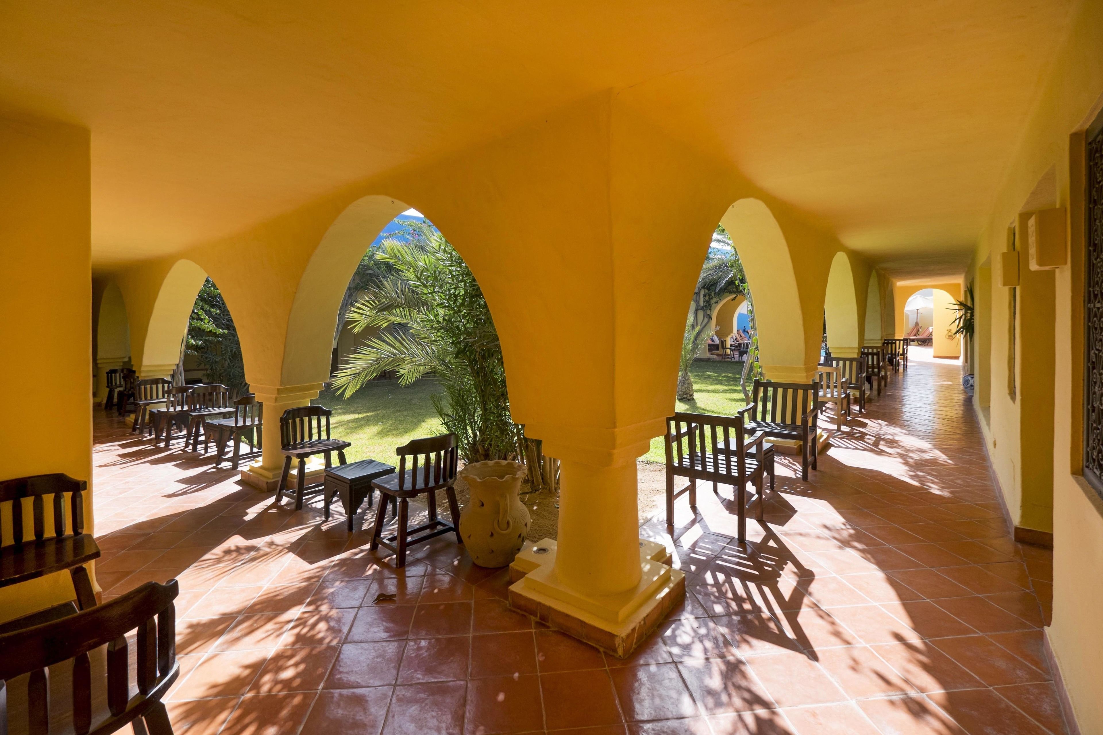 A covered outdoor area with tiled flooring, wooden benches, and arches.