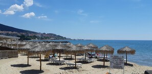 Uma praia com guarda-sóis de palha, espreguiçadeiras e uma placa.