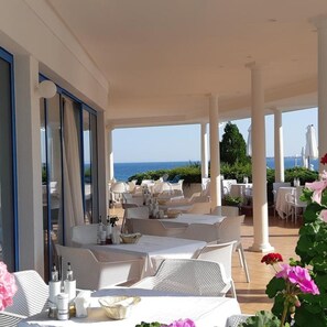 An outdoor dining area with tables and chairs, a view of the sea, and a covered structure with columns. - Primasol Sineva (Sveti Vlas)