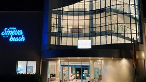 A hotel with a modern glass facade, a visible staircase, and a neon sign indicating the name 'Sineva Beach.' - Primasol Sineva (Sveti Vlas)