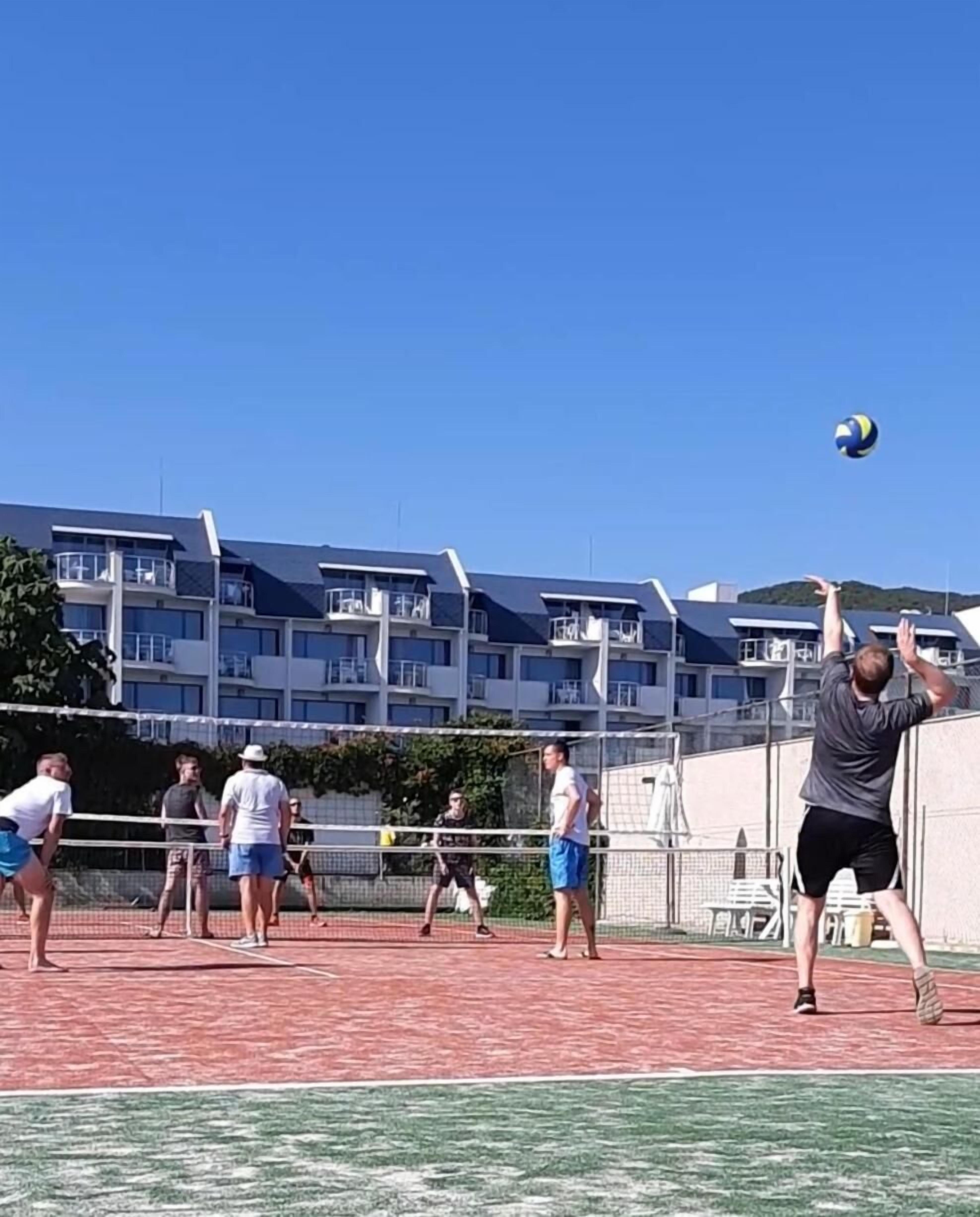 A volleyball court with players, a net, and a building in the background.