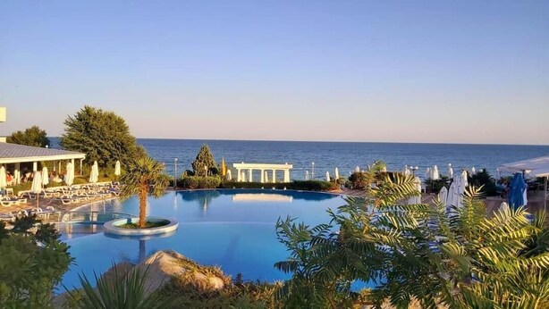 A pool with a view of the sea, surrounded by palm trees and a white gazebo. - Primasol Sineva (Sveti Vlas)