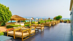 A sunlit outdoor seating area with wooden furniture and a pool in the background. - Karya Family Resort – All inclusive (Menderes)