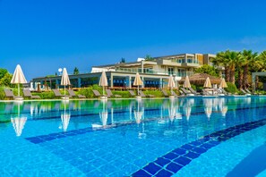 A swimming pool with lounge chairs and umbrellas, surrounded by a hotel building with balconies and palm trees. - Karya Family Resort – All inclusive (Menderes)