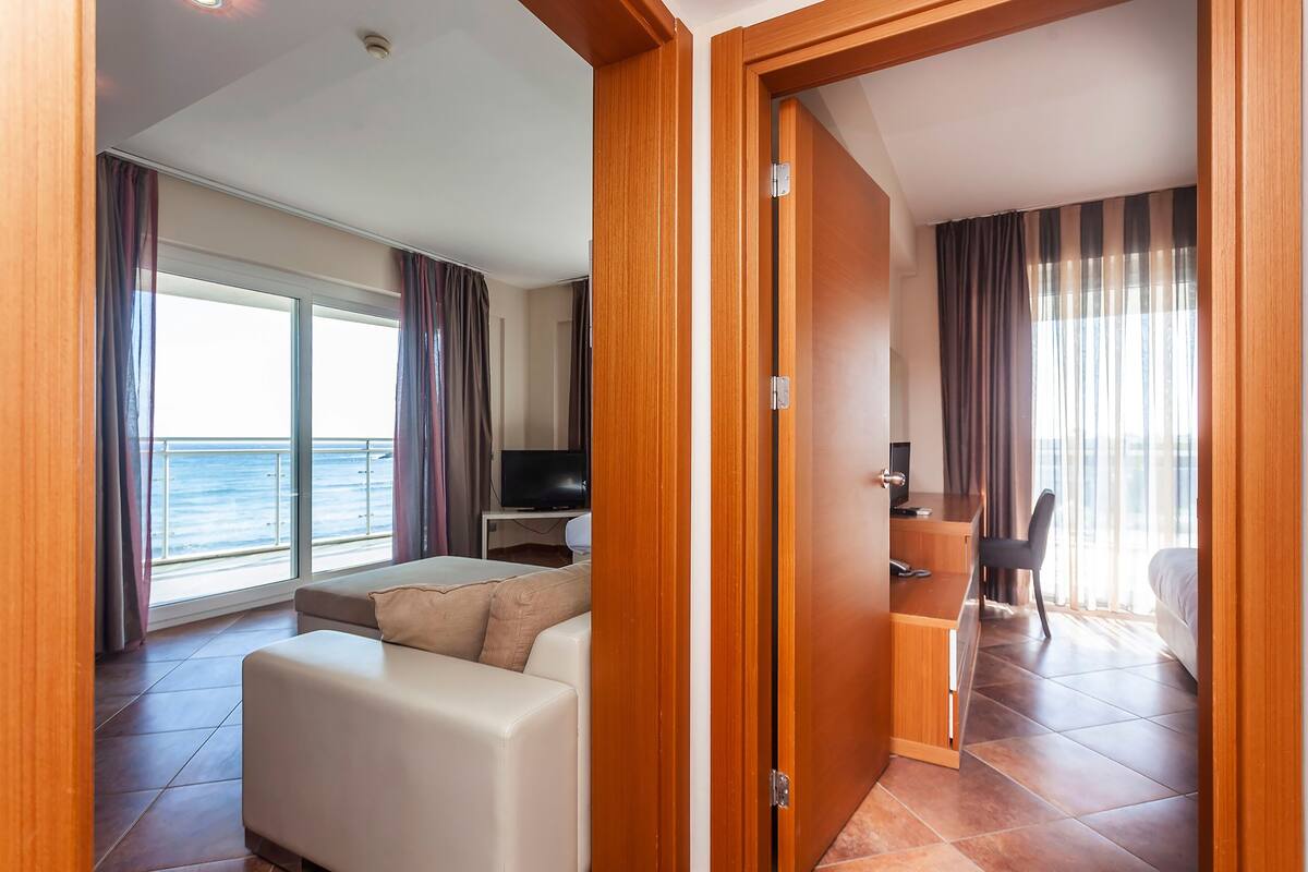 A modern hotel room with a sofa, a desk, a chair, and a TV.