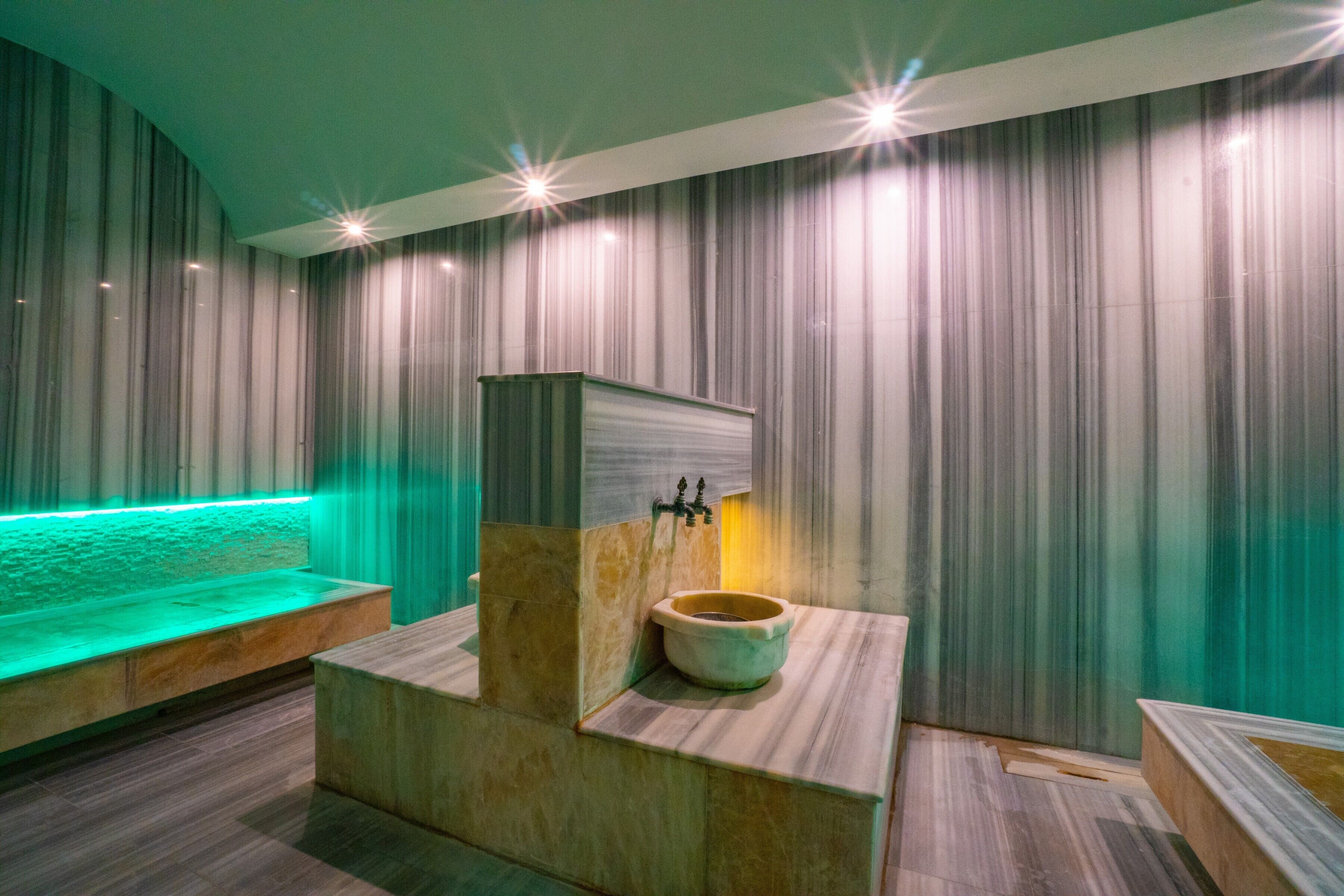 Een moderne badkamer met een marmeren wastafel, een bankje en een muur met groene verlichting.