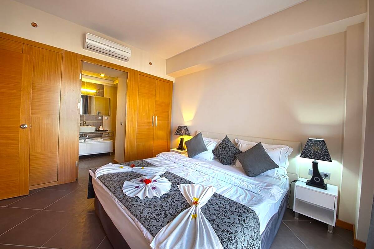 A hotel room with a large bed, a wardrobe, a bathroom with a sink and mirror, and two bedside lamps.