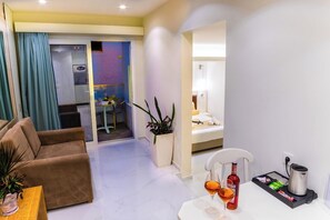 A hotel room with a sofa, a small table with a plant, a minibar, and a bathroom visible through a glass door. - W Suites (Hersonissos)