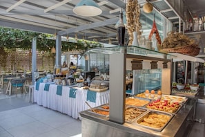 A buffet setup with various food items and a seating area with tables and chairs. - W Suites (Hersonissos)