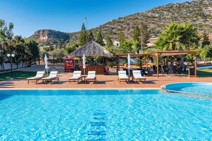 Una piscina con sillas de descanso y una zona sombreada, rodeada de vegetación y un paisaje montañoso.